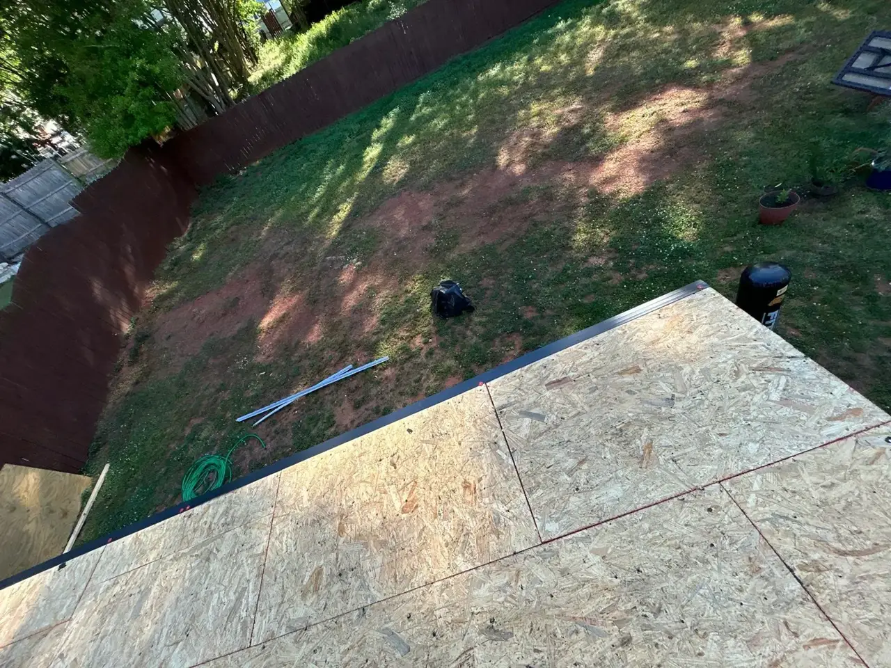 Newly installed roof decking overlooks a fenced backyard and scattered roofing tools