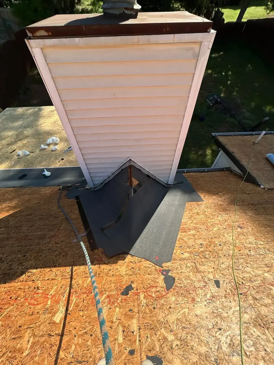 Roof replacement area with exposed decking, chimney siding, and black underlayment visible.