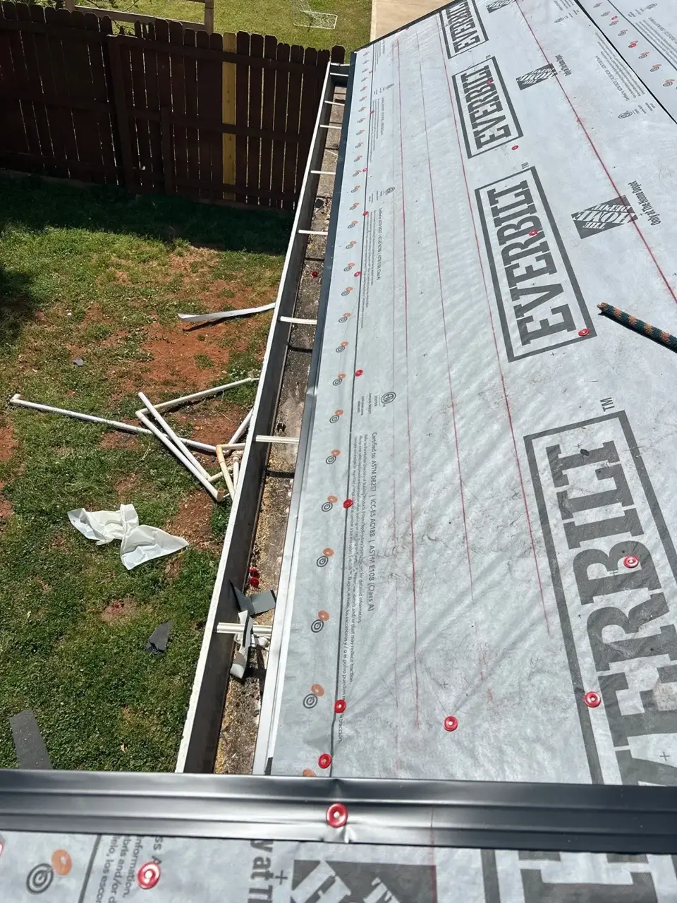 Roof edge covered with synthetic underlayment, metal flashing, and exposed yard below.