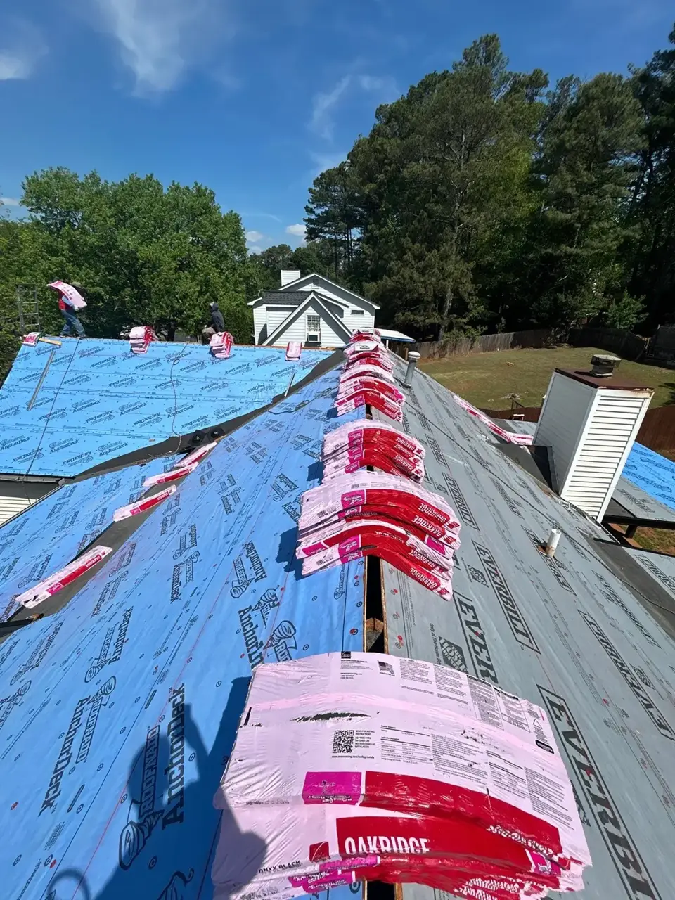 Roof covered with blue underlayment and stacked shingle bundles in Lawrenceville, GA.