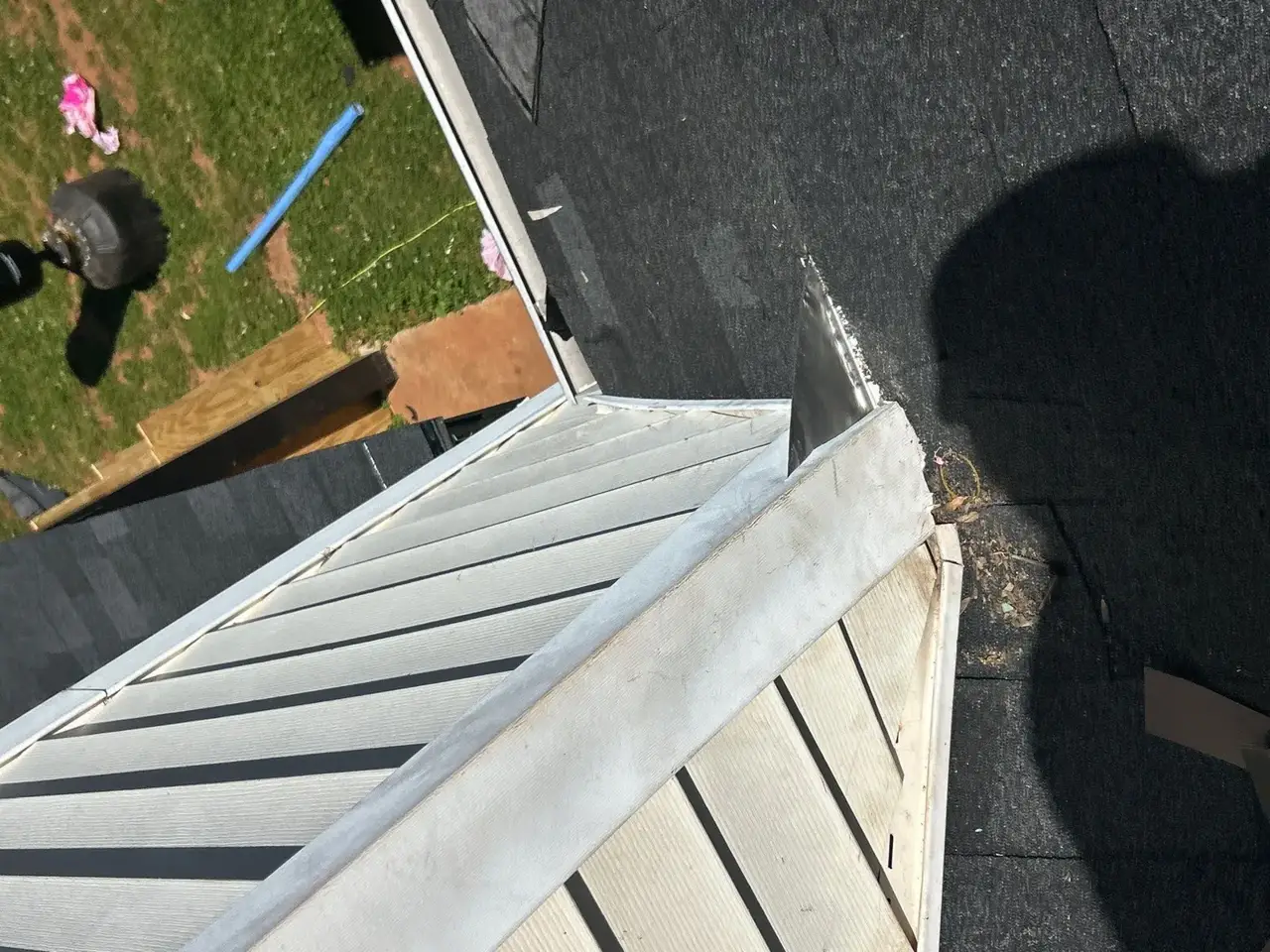 Roof valley with black underlayment, metal flashing, white siding, and yard visible below
