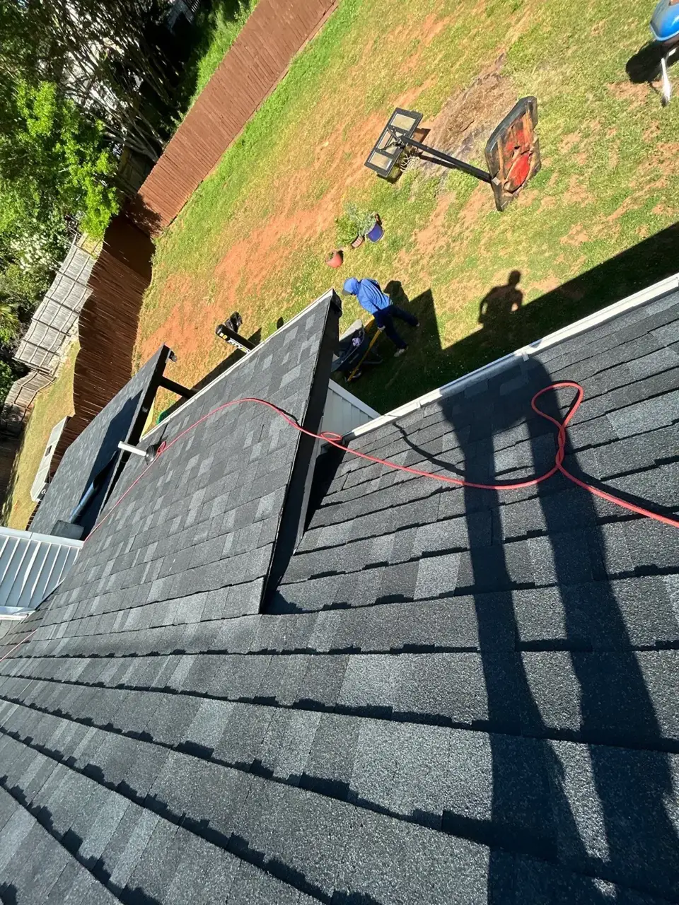 Dark shingle roof and workers below, with equipment and a red extension cord visible in Lawrenceville, GA