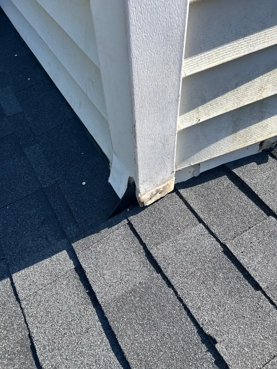 Close view of weathered siding trim meeting gray roof shingles at a chimney base.