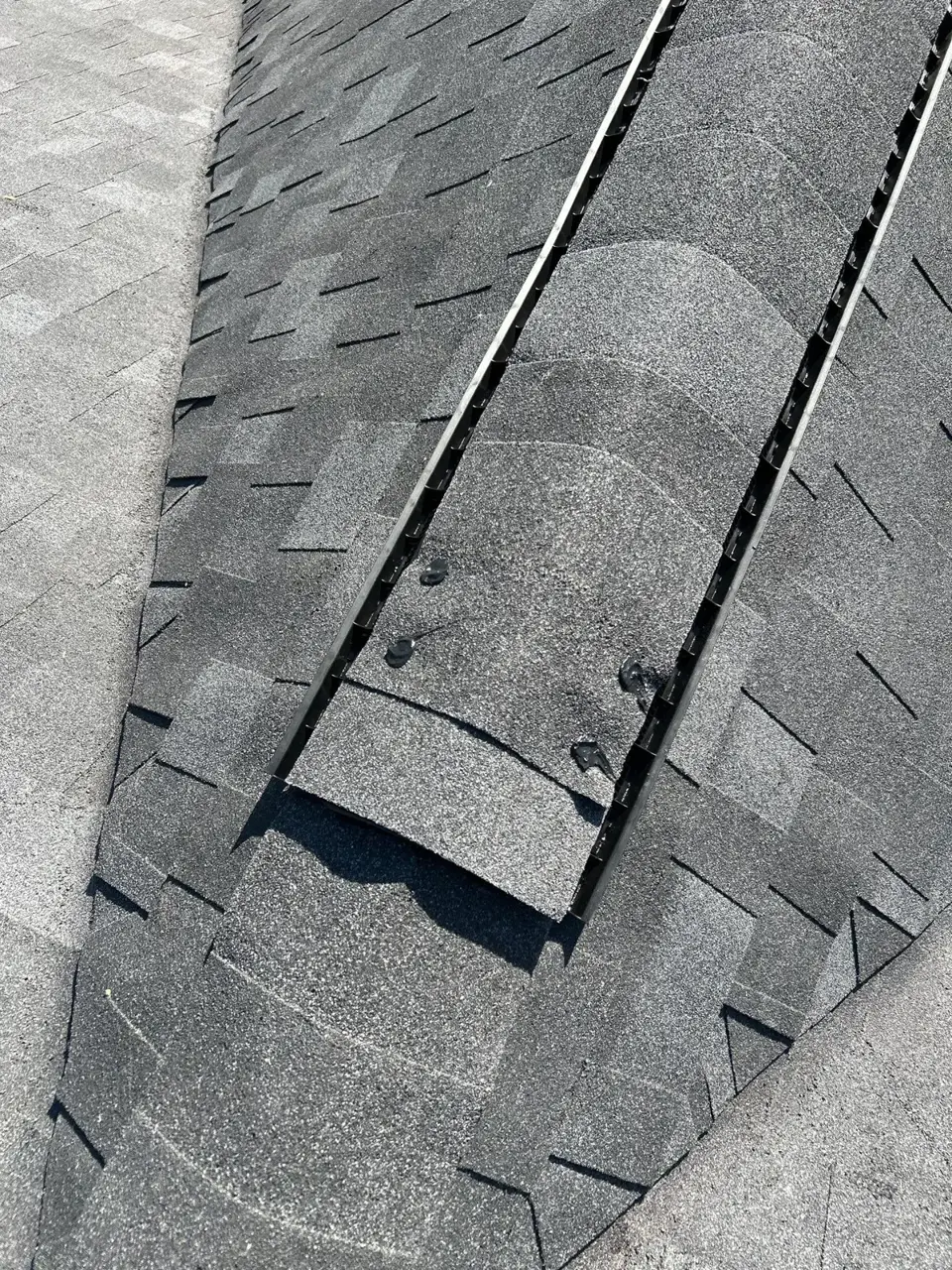 Gray asphalt shingles surround exposed ridge vent sections with loose or damaged shingle pieces.