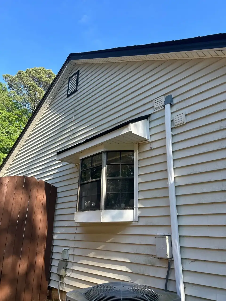 White-sided residential exterior in Lawrenceville GA shows a window, downspout, vents, and roof edge.
