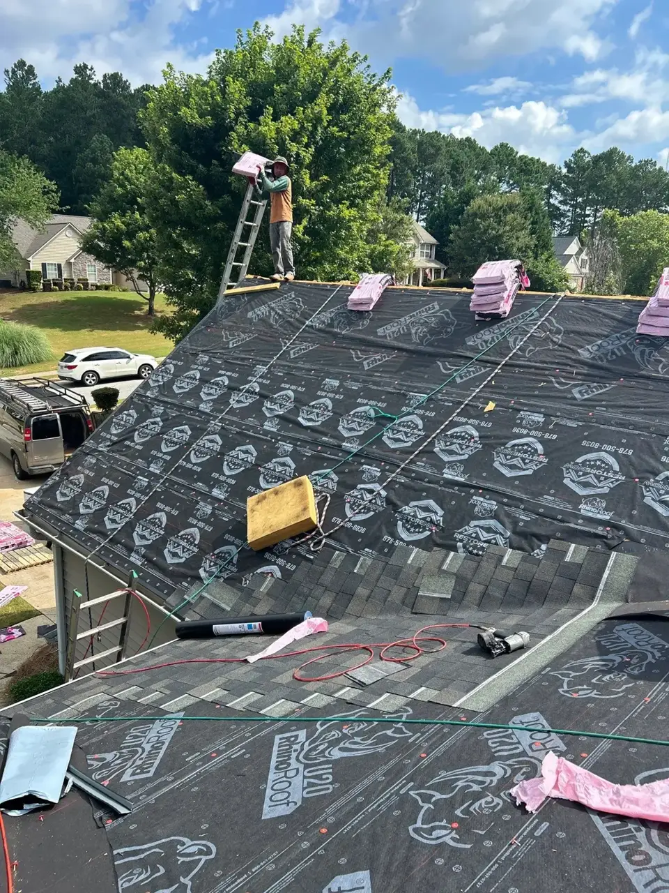 Roof replacement in Loganville GA shows underlayment, shingle bundles, tools, and worker on steep roof.