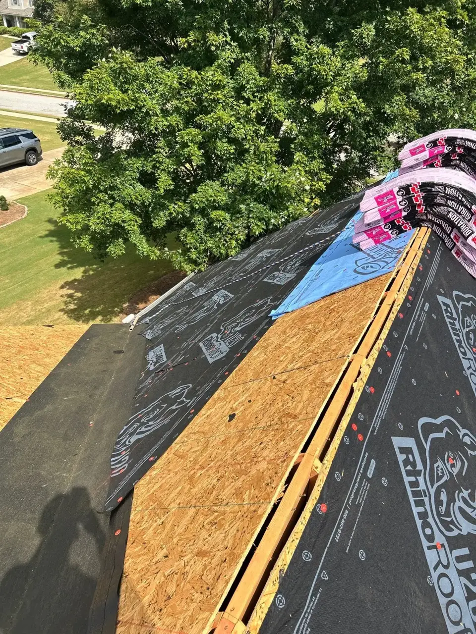 Roof replacement in Loganville GA exposes plywood decking beside black underlayment and stacked roofing materials.