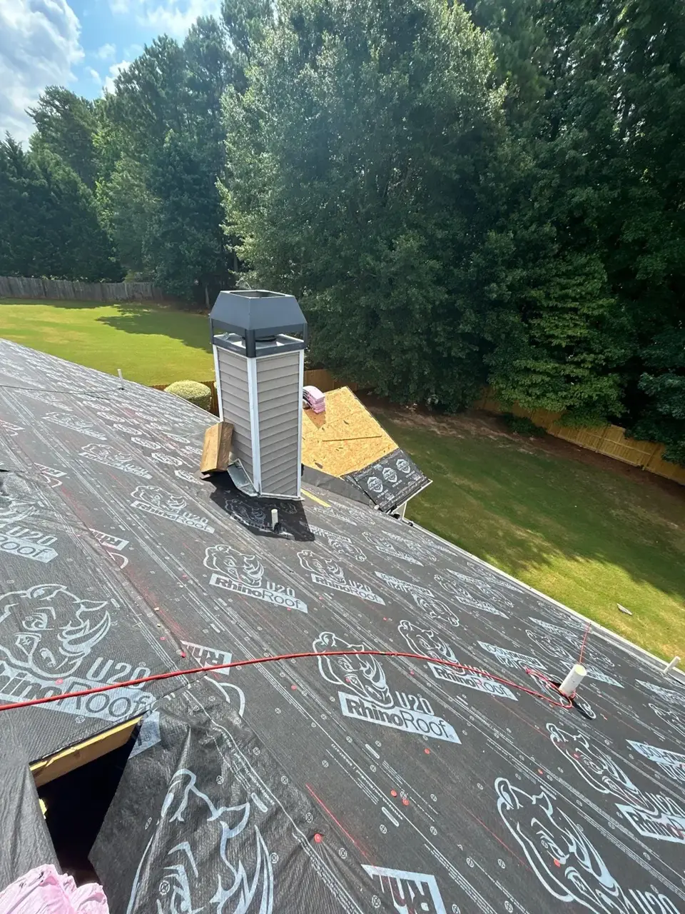 Roof replacement in Loganville GA shows black underlayment, chimney vent, exposed decking, and roofing tools.