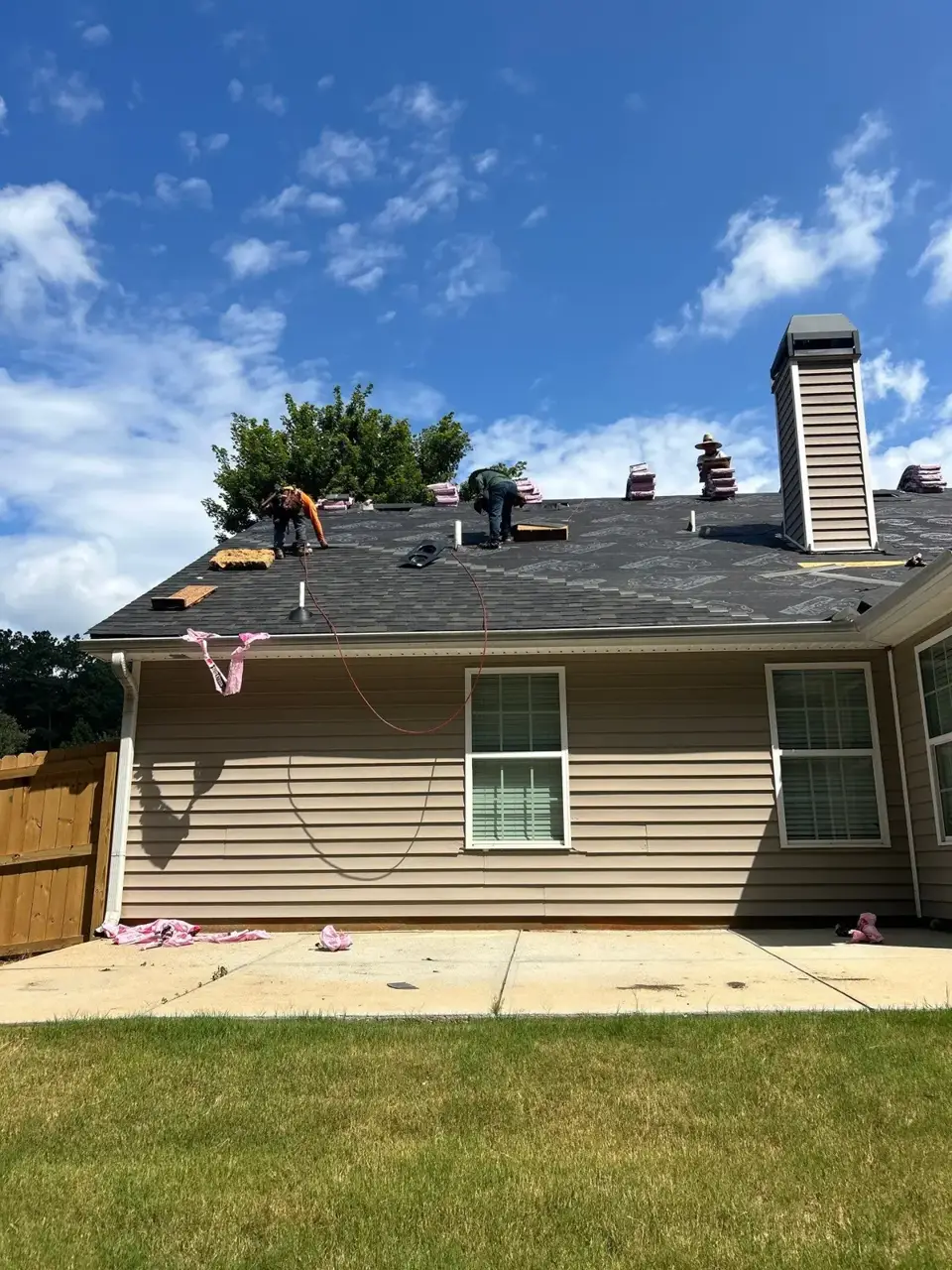 Residential roof with workers, shingle bundles, chimney vent, siding, and driveway in Loganville, GA