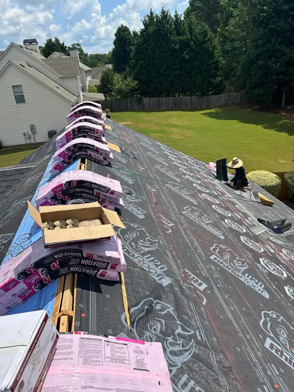 Roof covered with underlayment, stacked shingle bundles, and open shingle box overlooking a backyard