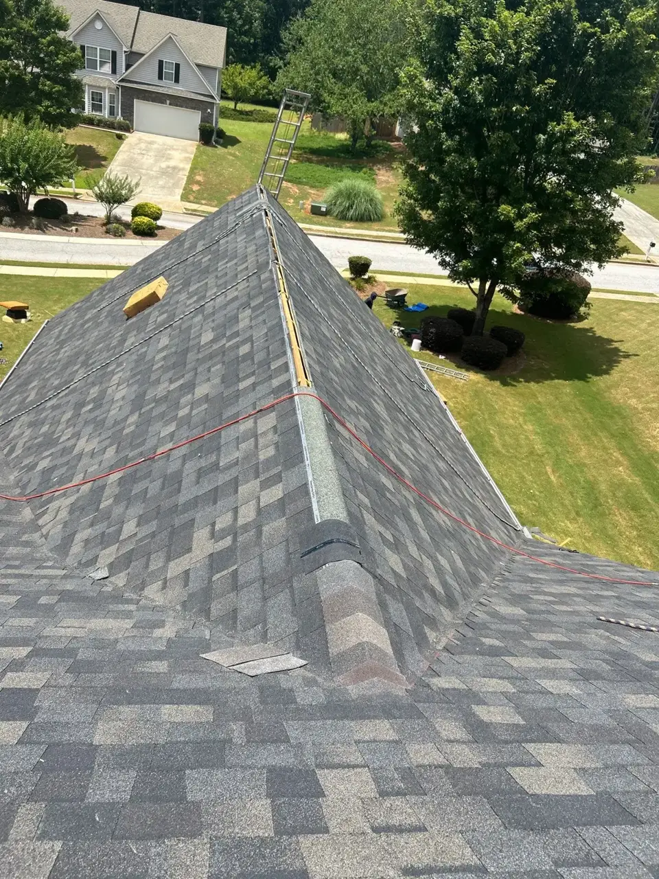 Gray shingle roof ridge with safety ladder, roof lines, and suburban homes in Loganville GA