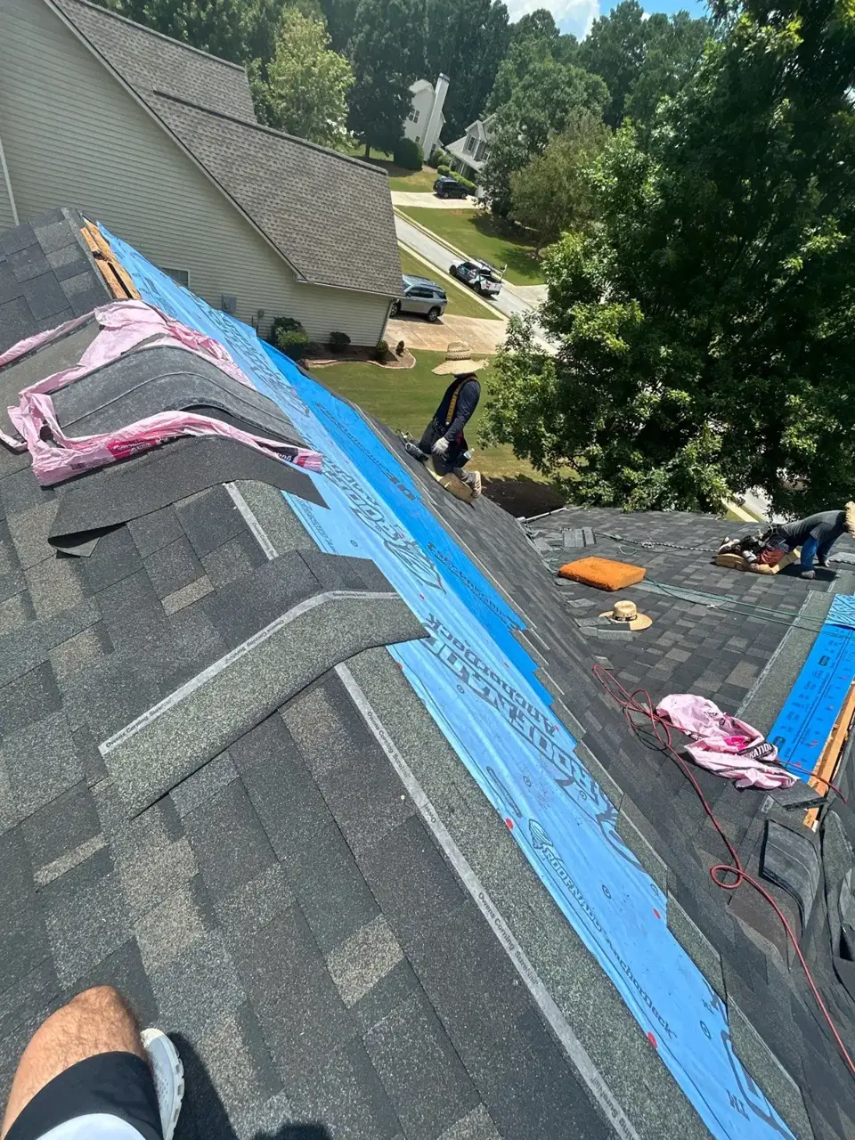 Roof replacement underway with blue underlayment, exposed decking, tools, and workers in Loganville GA