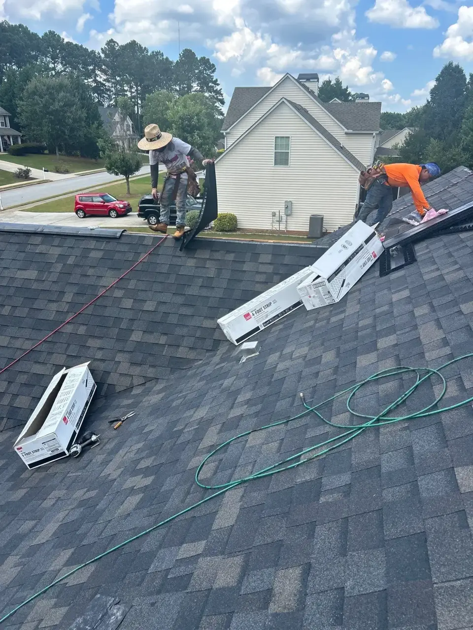 Roofing workers installing shingles beside open shingle boxes and coiled hoses in Loganville GA