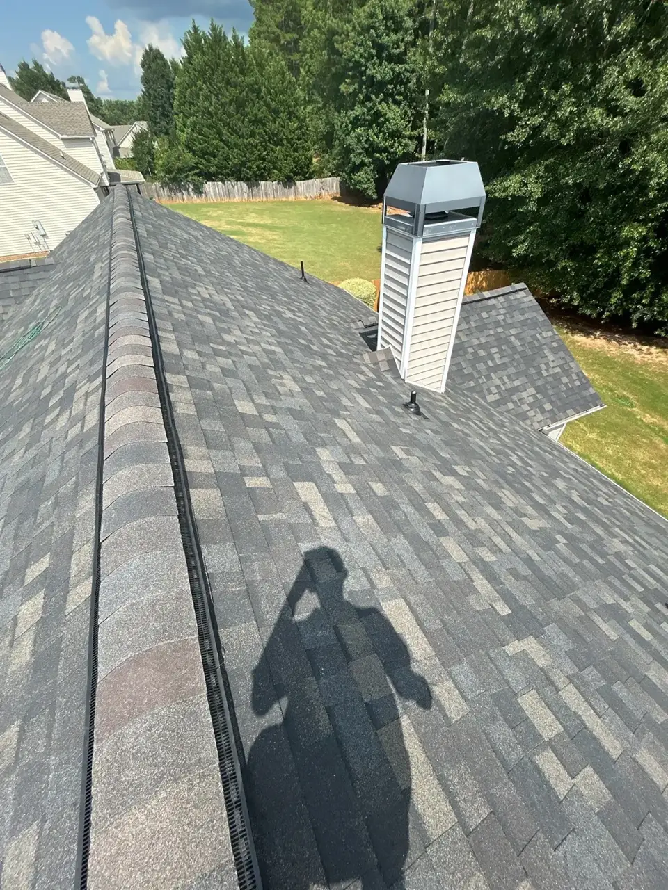 New gray shingle roof with ridge vent and chimney overlooking a backyard in Loganville GA.