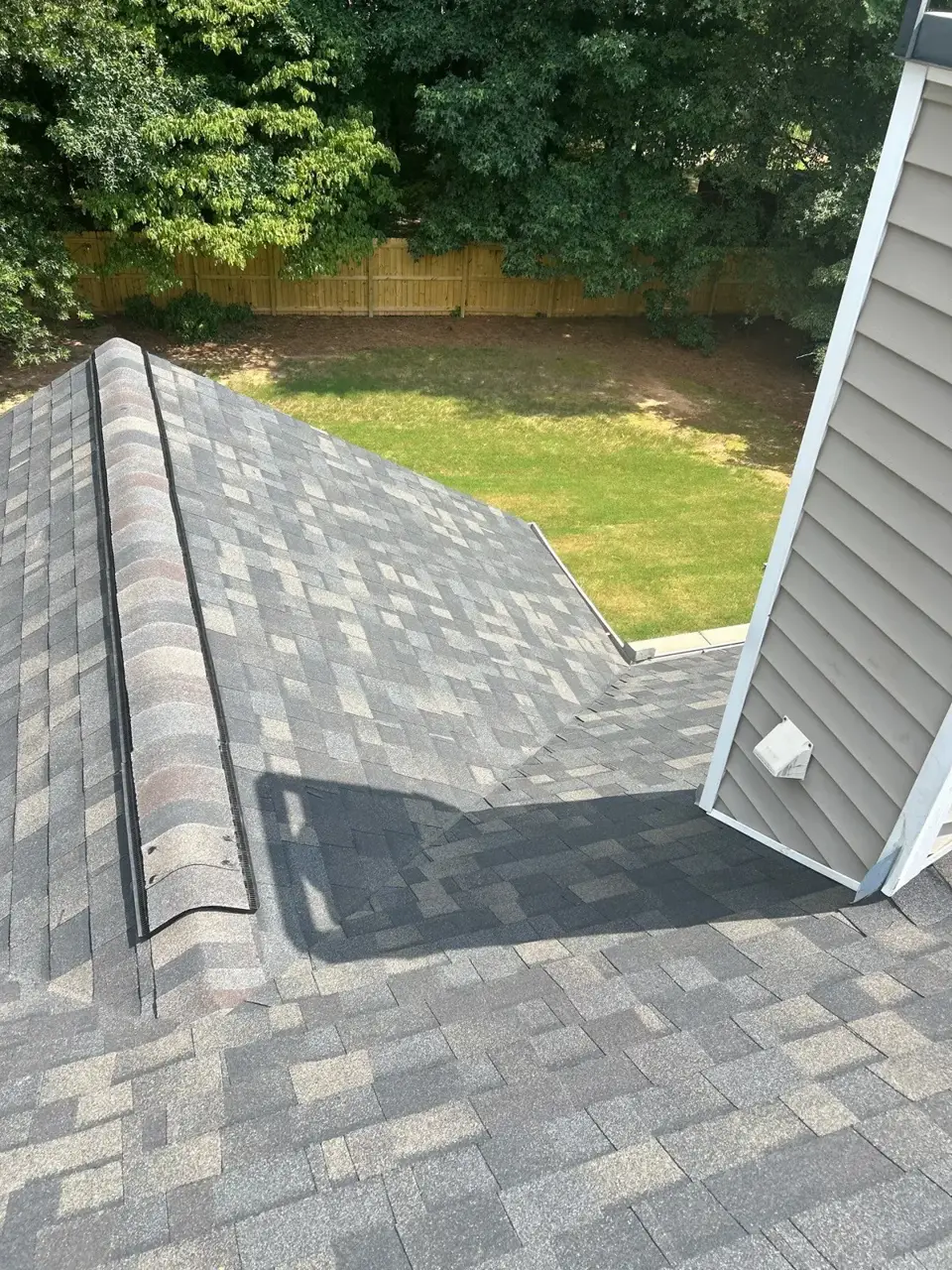 Gray shingle roof meeting vinyl siding, with ridge vent and backyard fence visible.