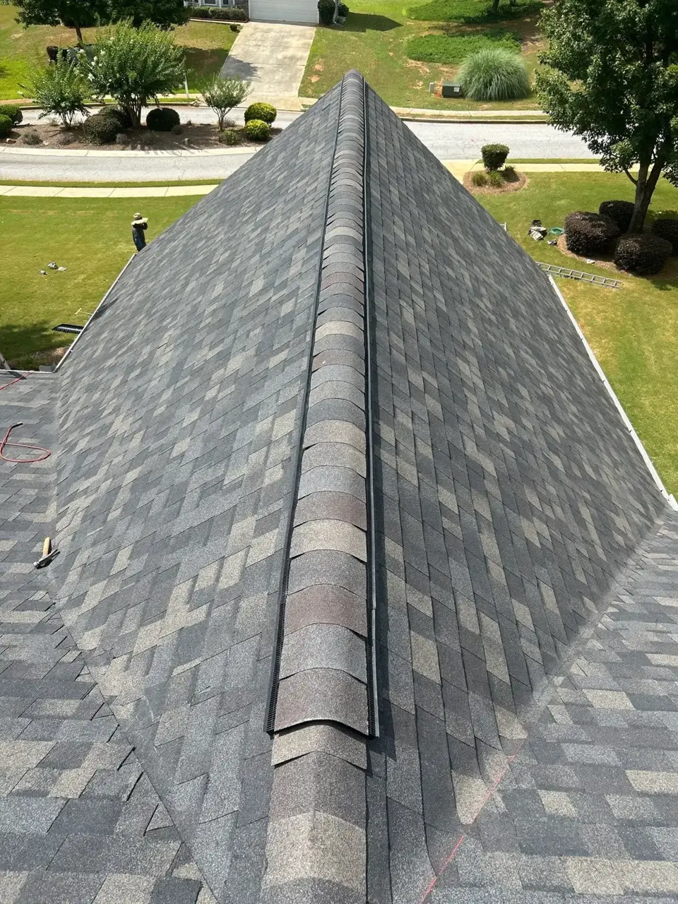 Completed gray shingle roof ridge viewed from above, with ladders and workers visible below in Loganville GA.