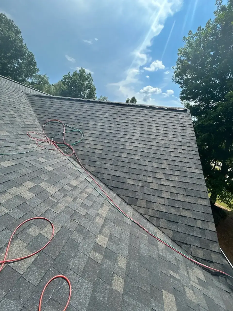 Gray shingle roof viewed closely with red and green roofing hoses across the surface.