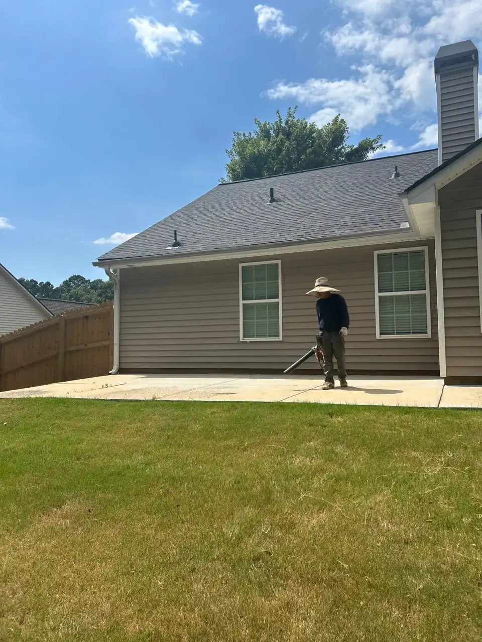 Back of a home with gray roof, beige siding, chimney, and worker on patio in Loganville, GA.