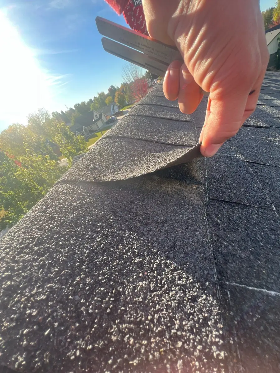 Worker lifting roof shingle near ridge during installation, Southern Premier Roofing work near Carl GA