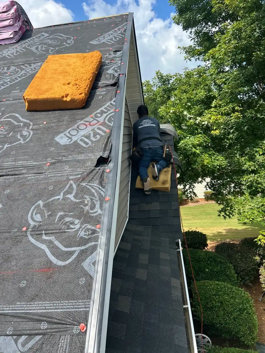 Roofer installing shingles along roof edge beside exposed underlayment, Southern Premier Roofing work near Lawrenceville GA