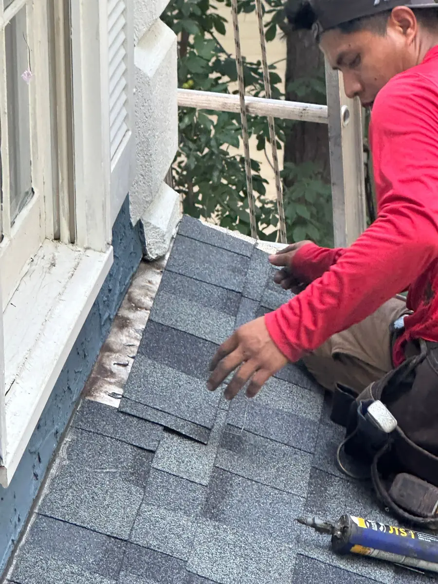 Worker placing shingle near wall flashing with roofing tools nearby, Southern Premier Roofing work near Monroe GA