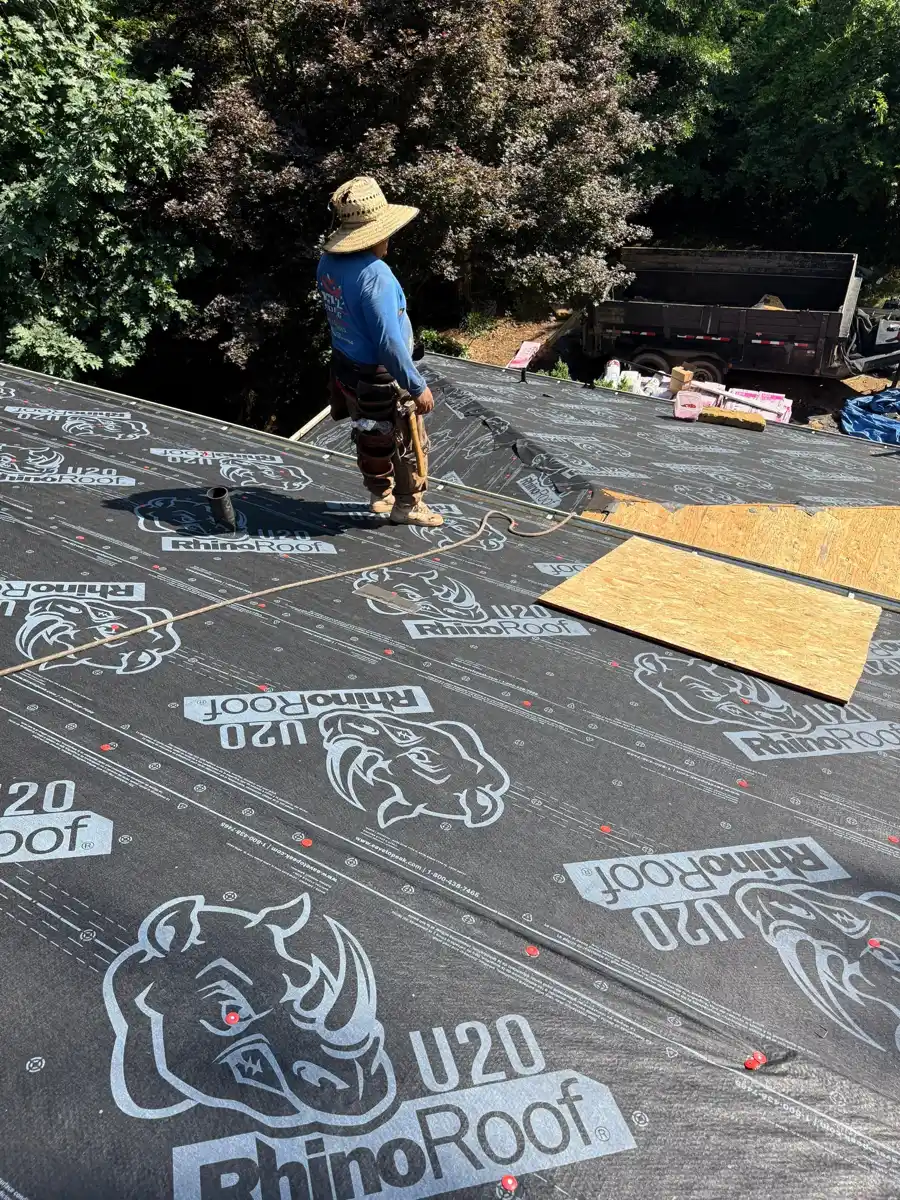 Worker installs printed roofing underlayment across roof deck, Southern Premier Roofing work near Pendergrass GA