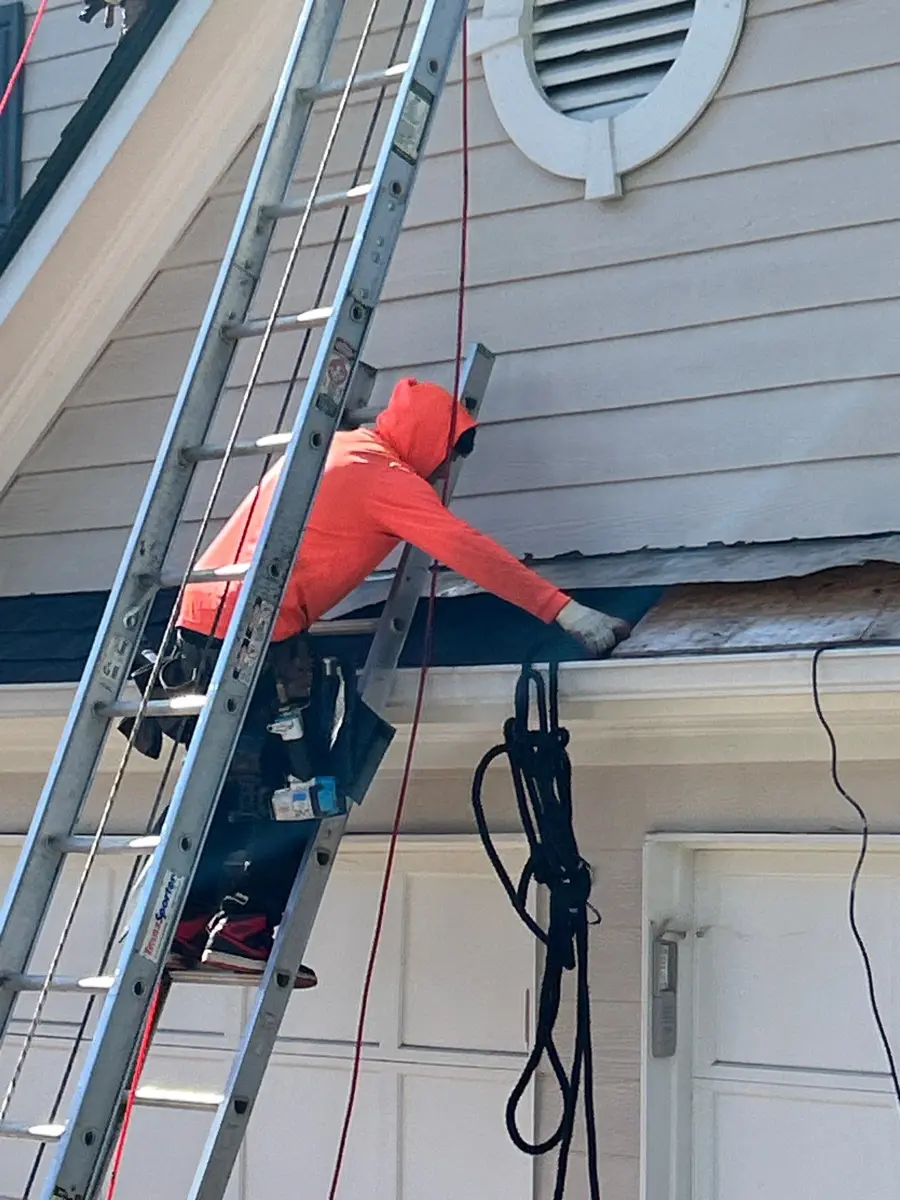 Worker repairing roof edge flashing beside ladder and exterior wall, Southern Premier Roofing work near Stone Mountain GA
