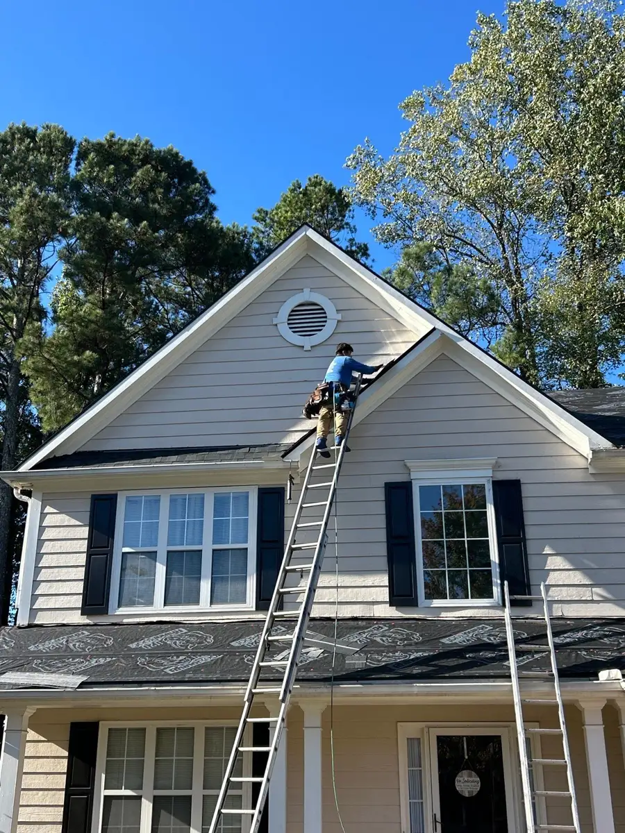 Worker installs shingles on steep gable roof using ladder, Southern Premier Roofing work near Tucker GA