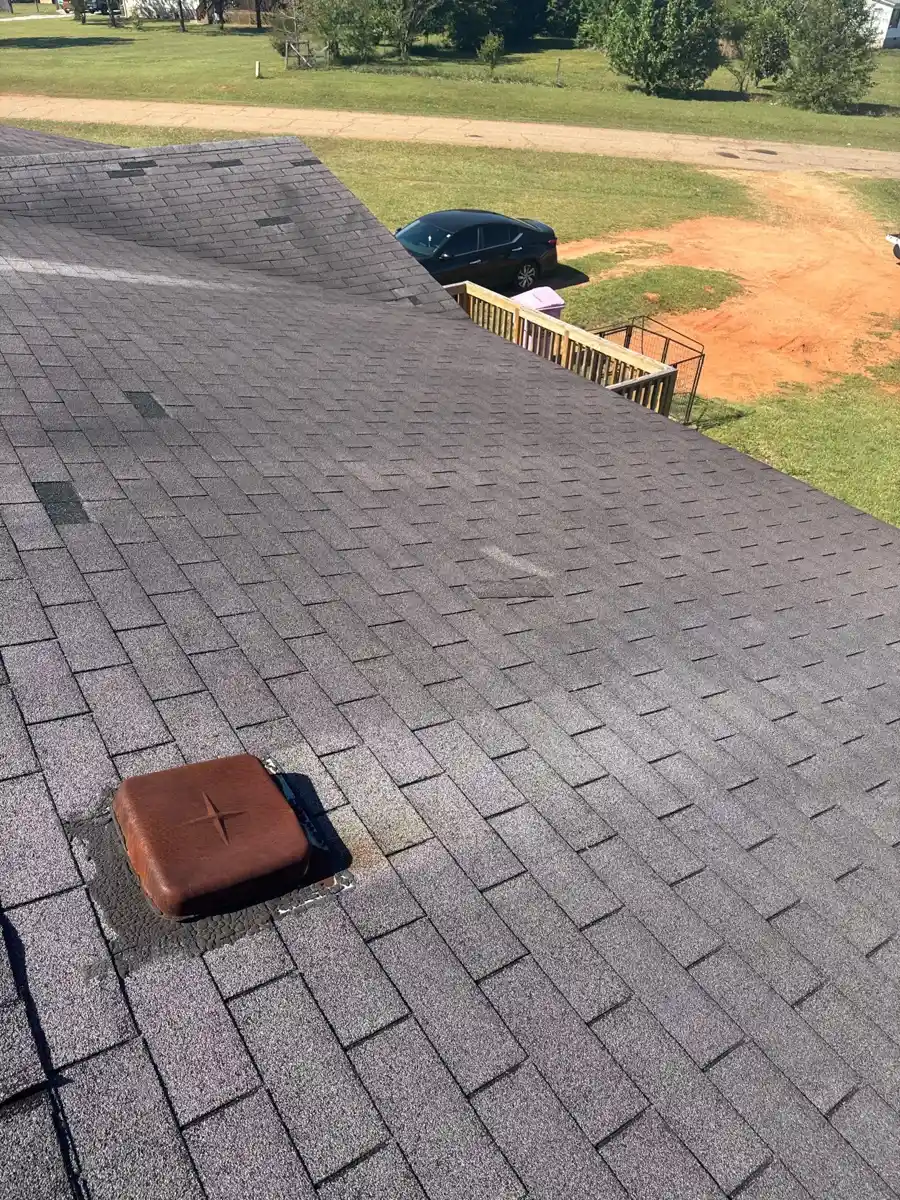Roof shingles show damaged patches beside a raised brown roof vent, Southern Premier Roofing work near Bishop GA