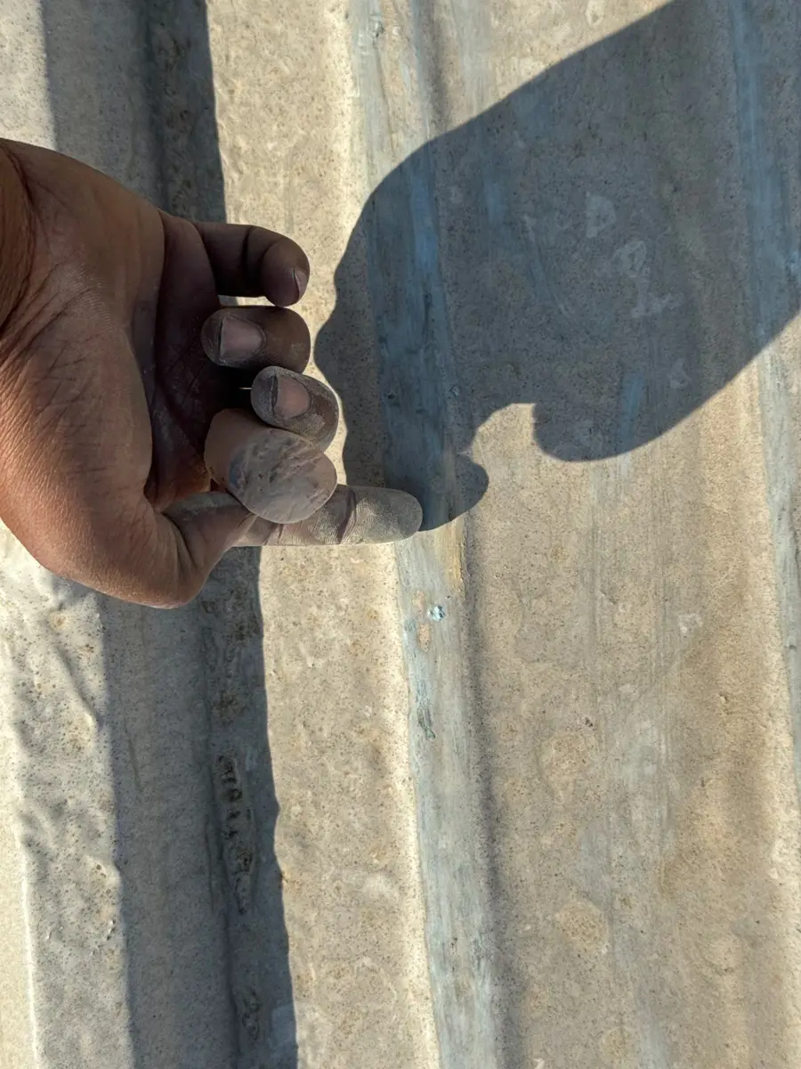 Hand points toward a damaged seam on a weathered roof panel, Southern Premier Roofing work near Braselton GA