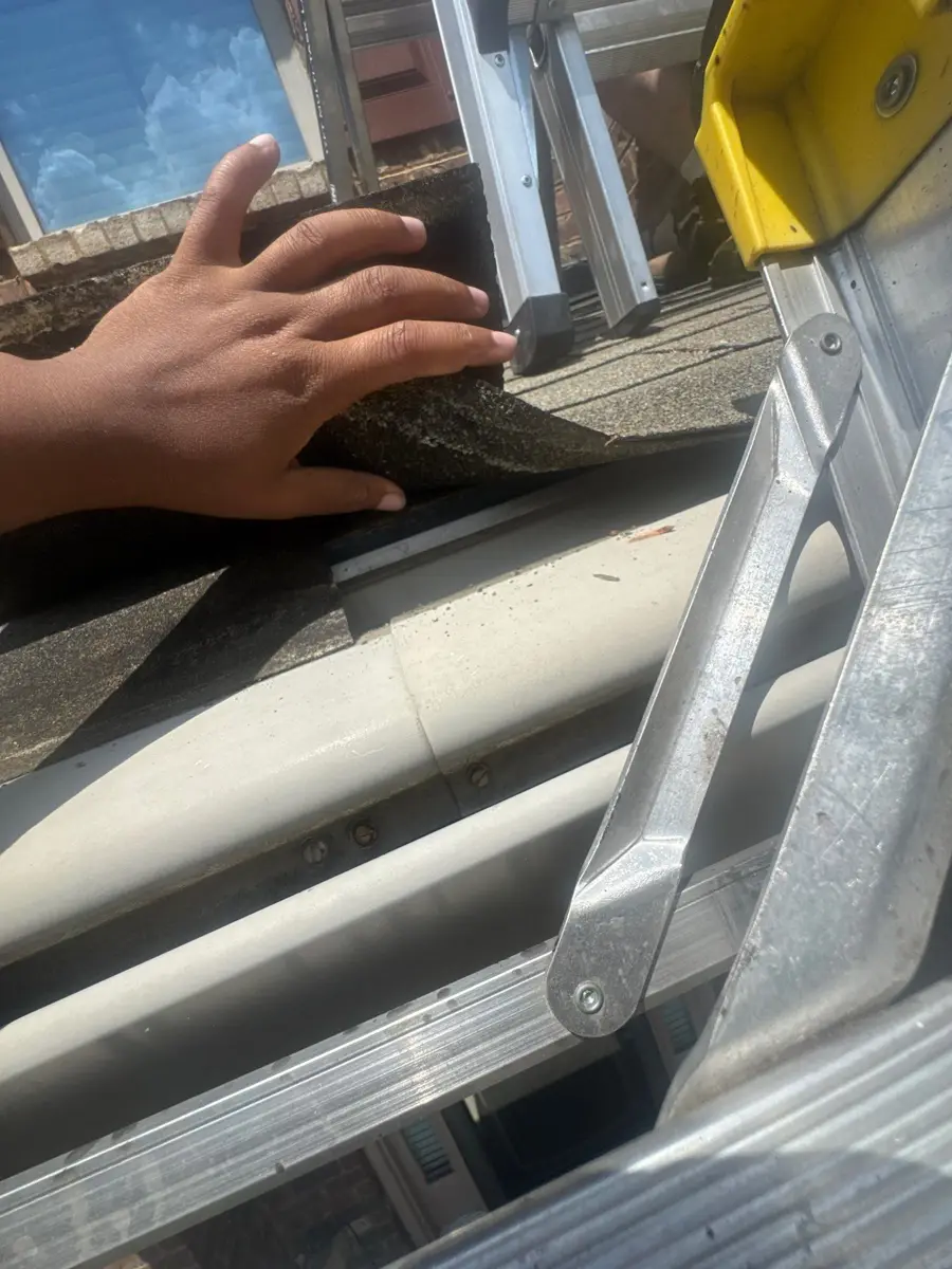 Hand inspecting roof edge flashing beside extension ladder, Southern Premier Roofing work near Gainesville GA