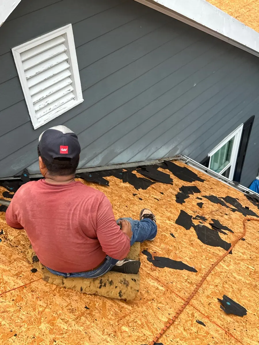 Worker kneels on exposed roof decking near house siding, Southern Premier Roofing work near Walnut Grove GA